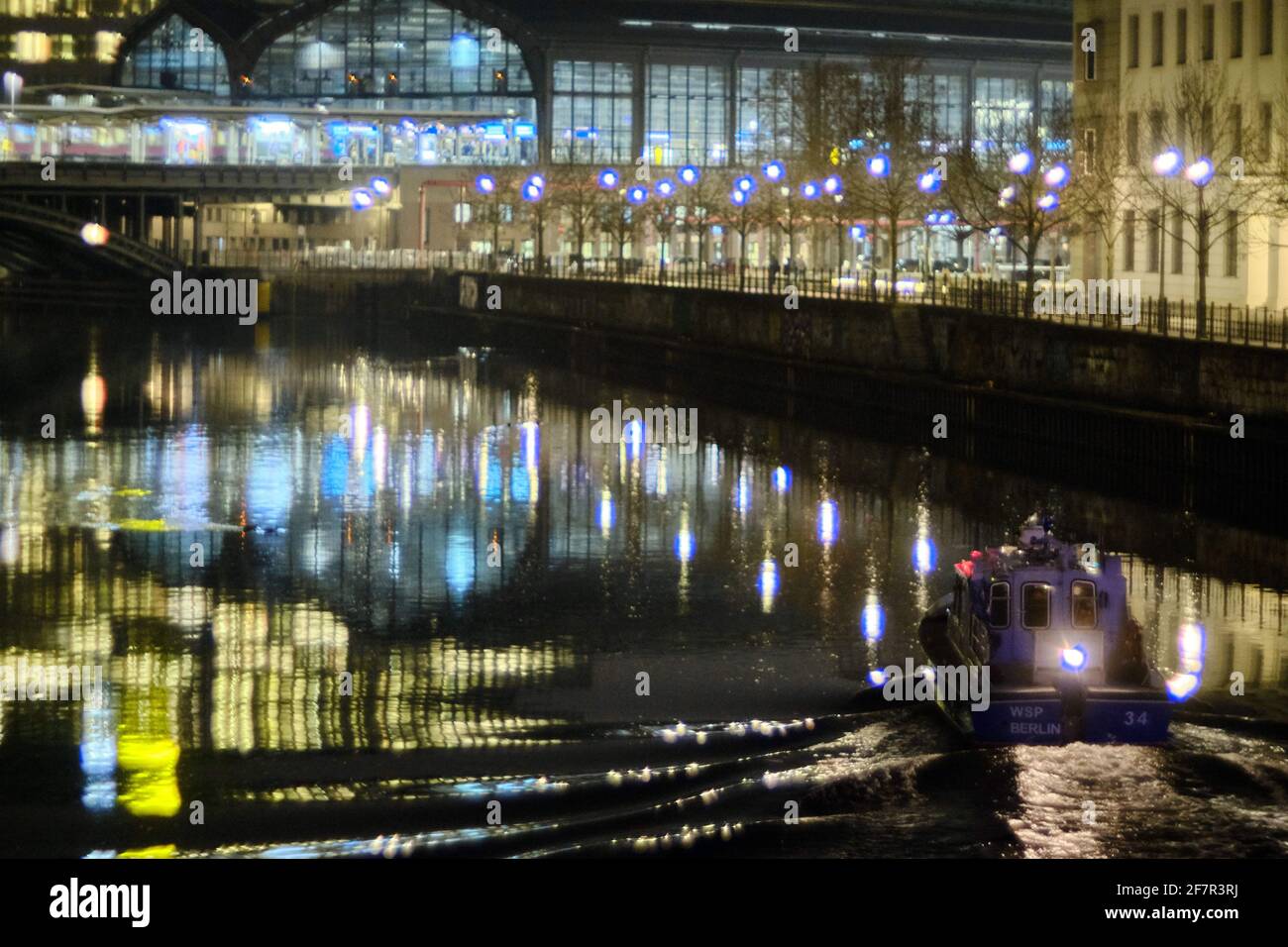 Berlino, Germania. 24 Marzo 2021. Le luci della stazione di Friedrichstraße si riflettono nel fiume Sprea, mentre una barca della polizia dell'acqua (WSP) pattuglierà in primo piano. Credit: Stefan Jaitner/dpa/Alamy Live News Foto Stock