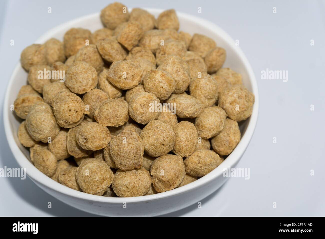 Un primo piano di bocconcini di soia in una ciotola con sfondo bianco. I nocciole di soia sono una fonte ricca di proteine specialmente per i vegani. Foto Stock