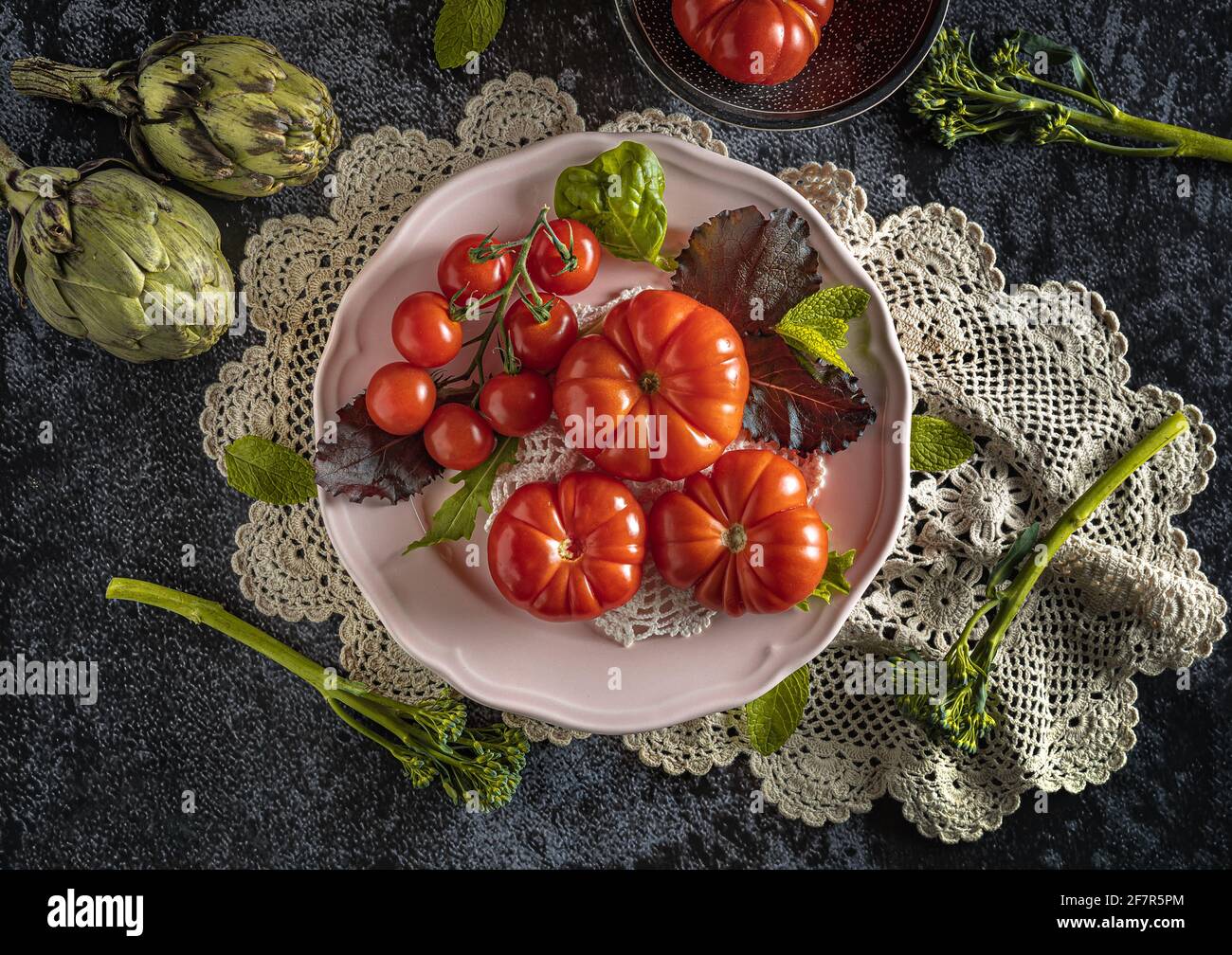 Moody fotografia di cibo scuro di pomodori raf freschi, bimi e carciofi. Immagine piatta con un aspetto vintage e uno sfondo nero. Foto Stock