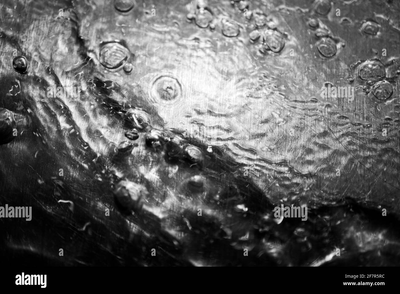 Bagnare l'acqua con bolle su una superficie metallica lucida Foto Stock