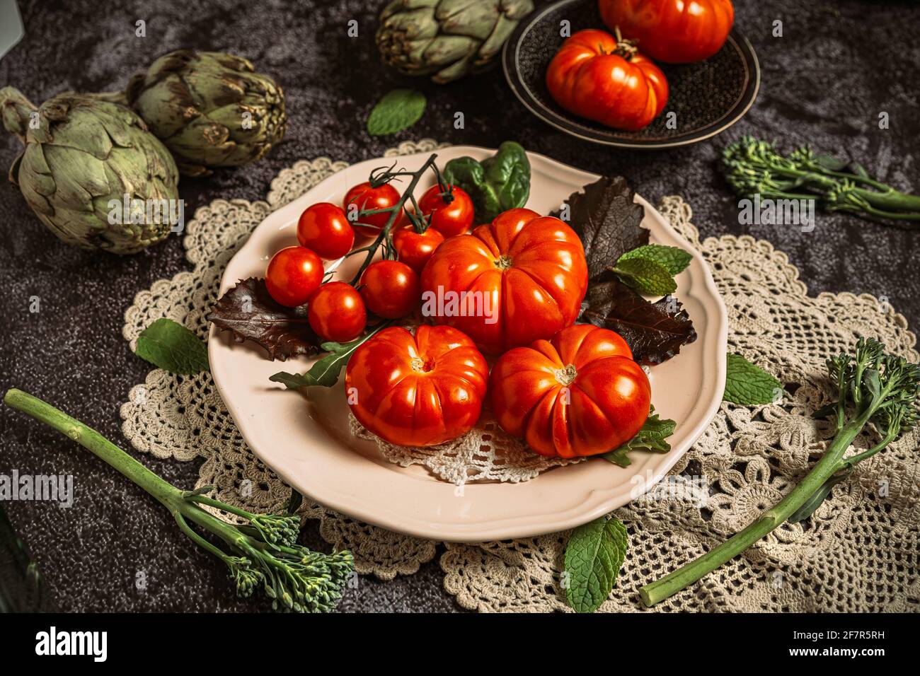 Moody fotografia di cibo scuro di pomodori raf freschi, bimi e carciofi. Immagine di natura morta con un aspetto vintage e uno sfondo nero. Foto Stock