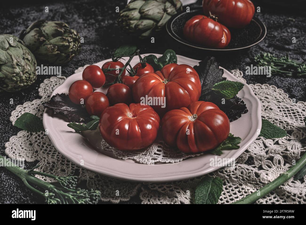 Moody fotografia di cibo scuro di pomodori raf freschi, bimi e carciofi. Immagine di natura morta con un aspetto vintage e uno sfondo nero. Foto Stock