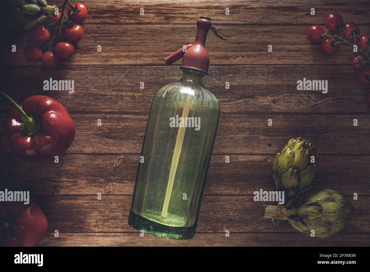 Foto di un antico sifone di soda, pomodori ciliegini freschi, posate antiche, carciofi e pepe rosso su un tavolo di legno. Ancora li Foto Stock