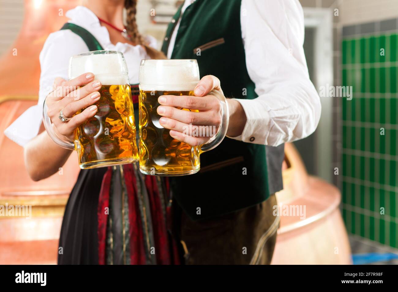 Uomo e donna con bicchieri da birra in Baviera tracht in birreria di fronte ad un bollitore brew Foto Stock