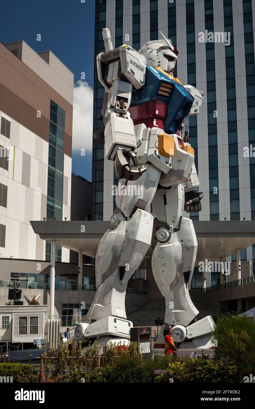 Vista verticale ad angolo basso di una donna che passa dall'enorme e impressionante statua unicorno Gundam a grandezza naturale in Divercity Tokyo Plaza, Odaiba Island, Tokyo Foto Stock