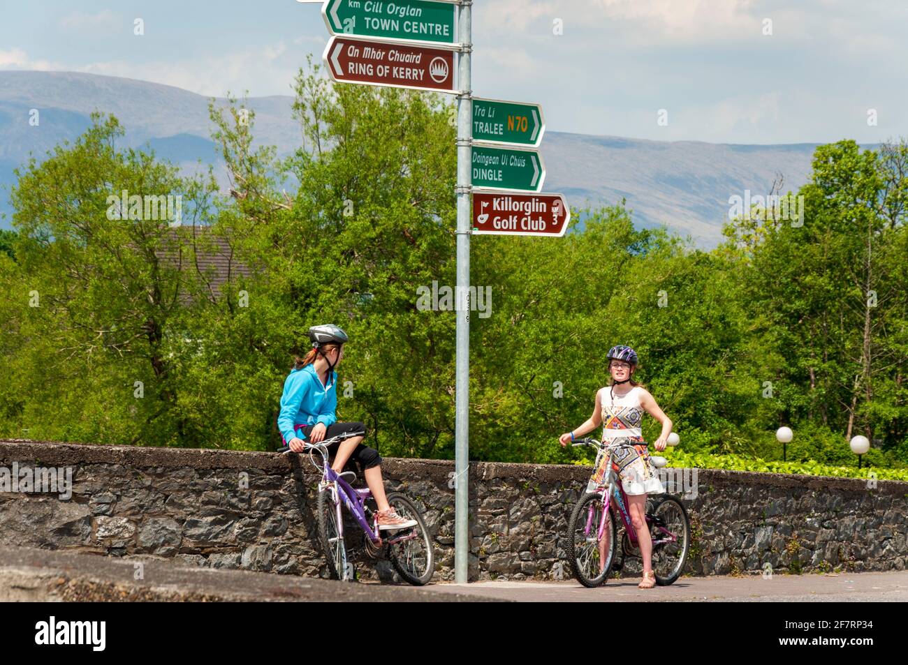 Cartelli stradali bilingue all'incrocio del ponte Killorglin e due ciclisti turisti donne che si chiedono direzione, Killorglin, County Kerry, Irlanda Foto Stock