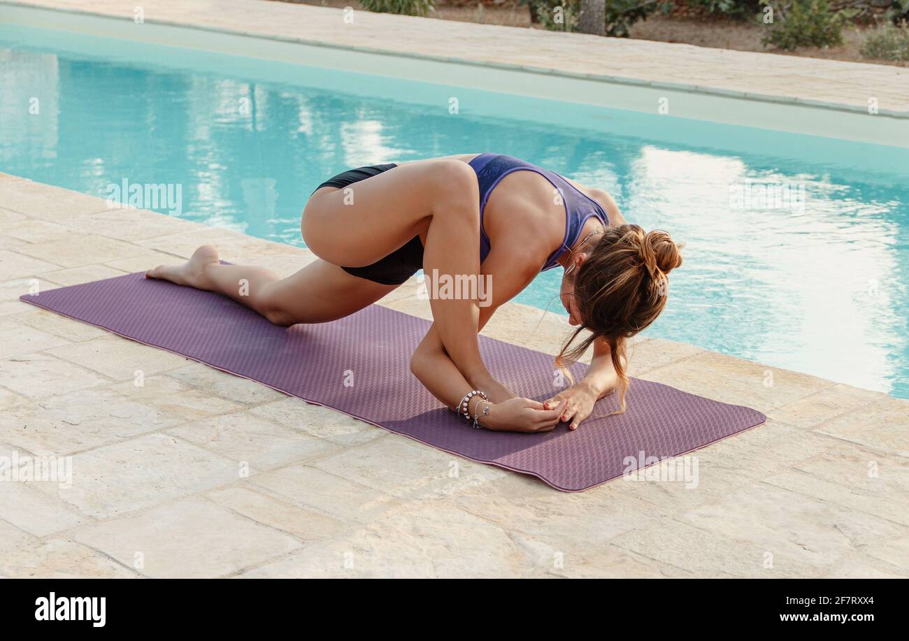 Giovane donna che pratica stretching in testa a ginocchio posa vicino una piscina Foto Stock