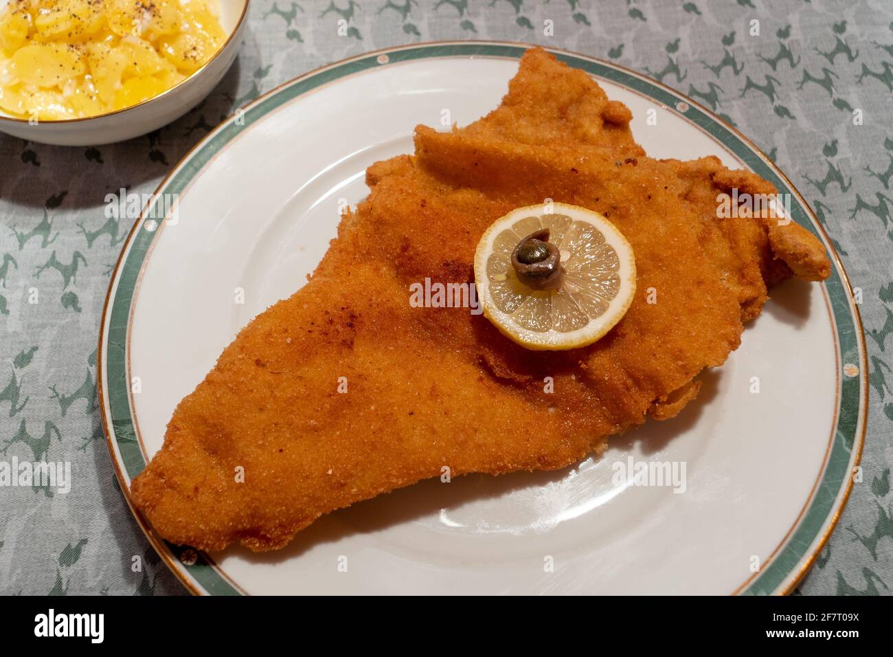 Wiener Schnitzel, un Escalope di vitello fritto viennese con insalata di patate, guarnito con una ruota al limone, un anello di anchovy e un cappero Foto Stock