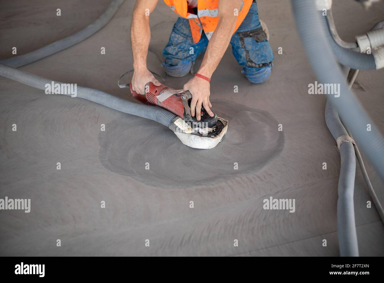 Lavoratore che lavora sul pavimento di un edificio industriale. Lavoratore di costruzione che produce grout e rifinendo pavimento bagnato di calcestruzzo. Foto Stock
