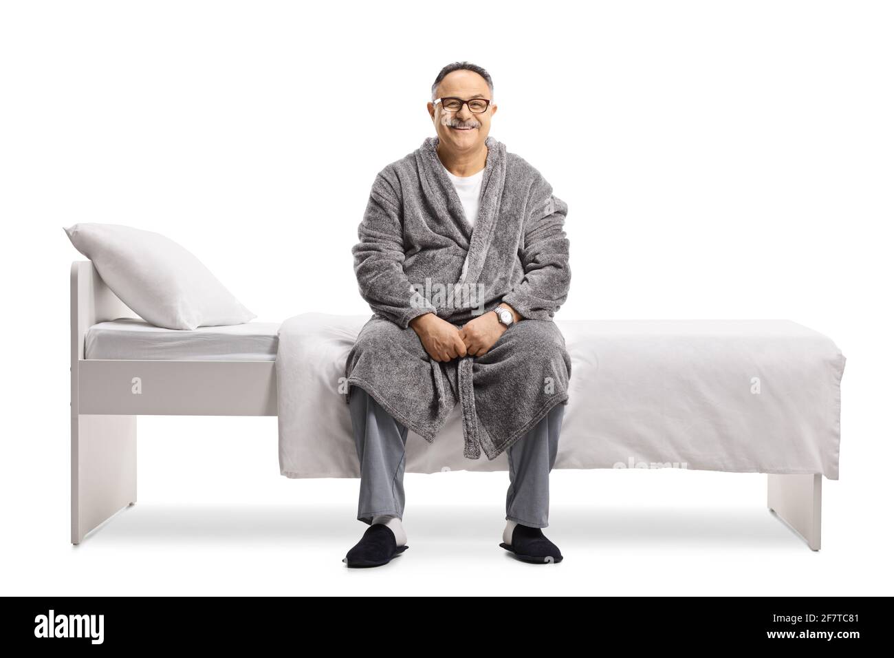 Uomo maturo in pigiama e un accappatoio seduto su un letto isolato su sfondo bianco Foto Stock