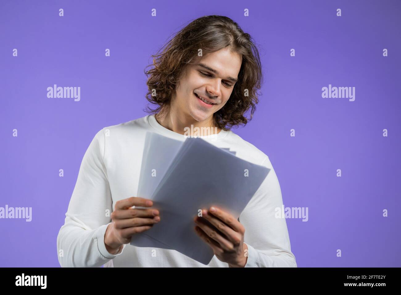 Uomo bello giovane controlla documenti, bollette di servizio, rapporto. Ragazzo isolato su sfondo viola. È soddisfatto Foto Stock