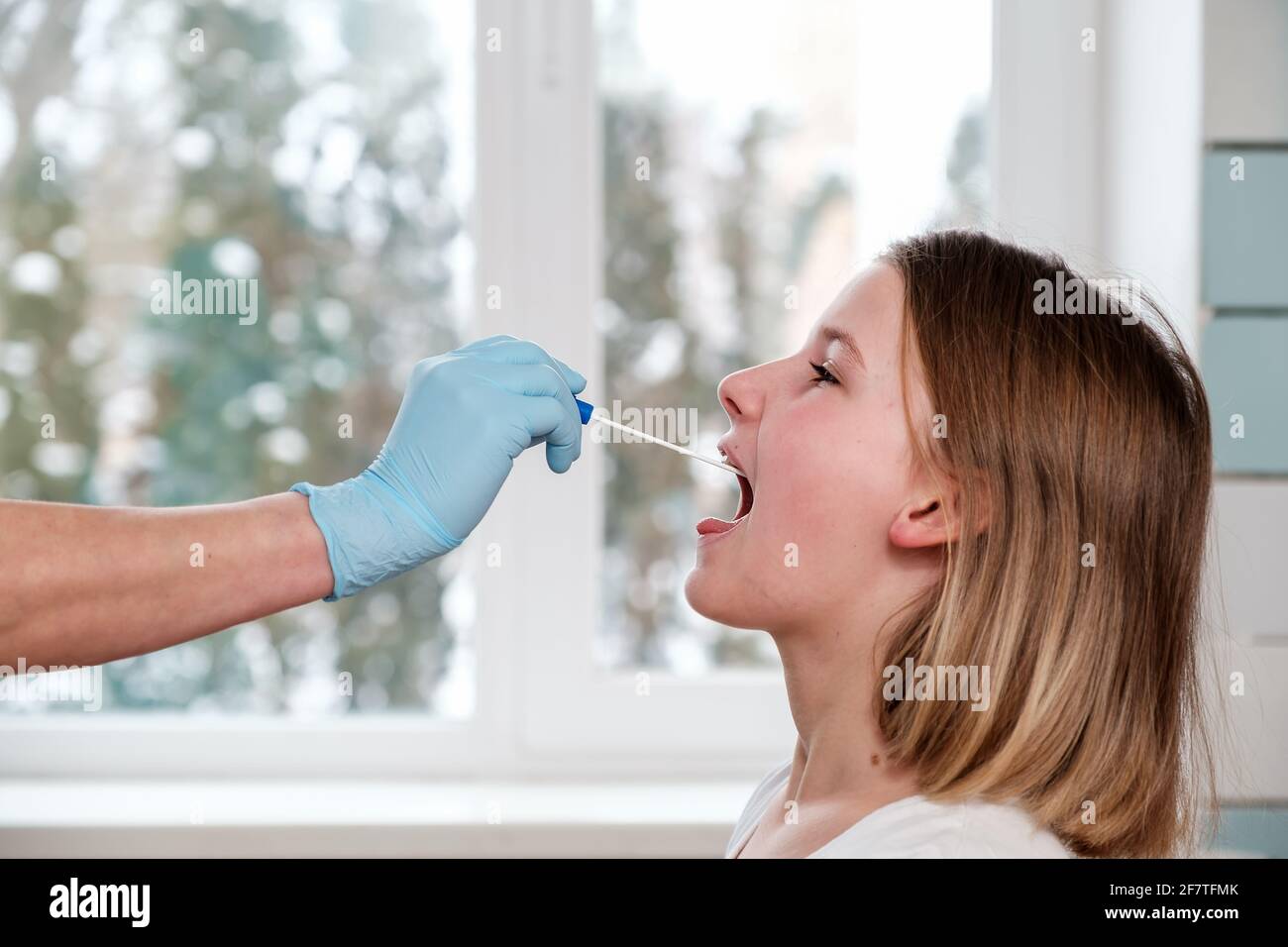 La mano del medico con un bastoncino di cotone prende un'analisi dalla bocca di una ragazza. Foto Stock