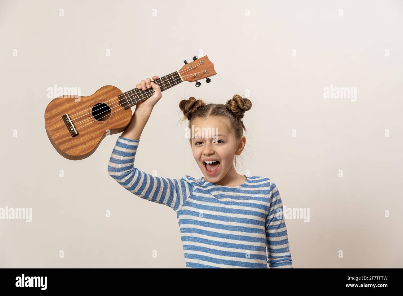 La ragazza canta e suona l'ukulele. Il bambino ride, si pone per la macchina fotografica e gode la musica. Imparare a giocare ukuleles Foto Stock