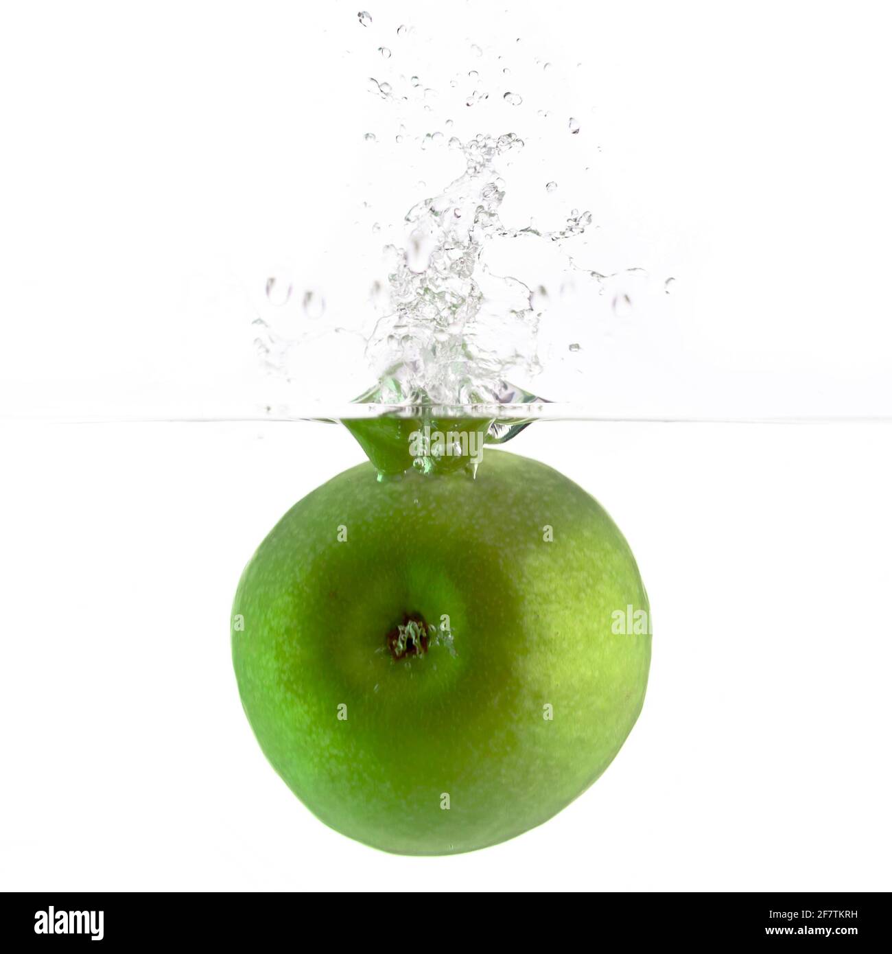 una mela verde che cade in acqua su uno sfondo bianco con schizzi, gocce e bolle Foto Stock