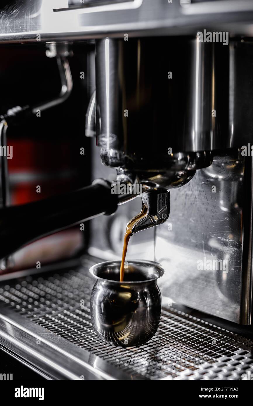 Primo piano della macchina da caffè professionale. Erogazione dell'espresso. Il barista prepara un delizioso caffè caldo Foto Stock