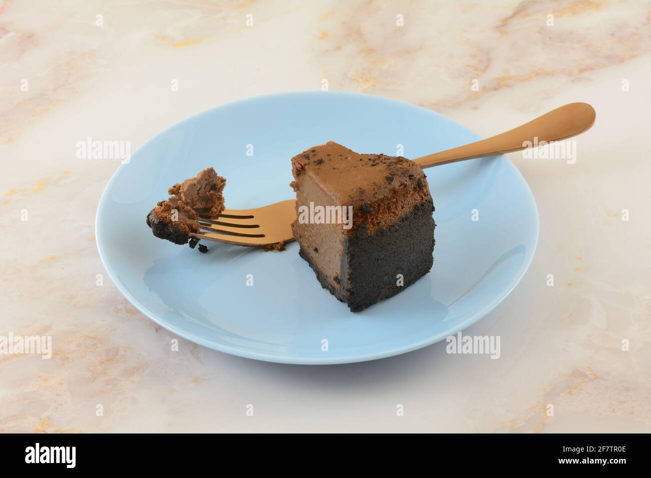 Fetta di cheesecake al cioccolato belga con morso e rame mancanti forchetta su piatto da dessert blu Foto Stock