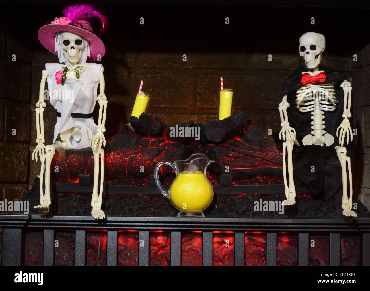 Festa di limonata scheletro in angolo di inferno con camino bruciante con coppia, bicchieri limonata e caraffa Foto Stock