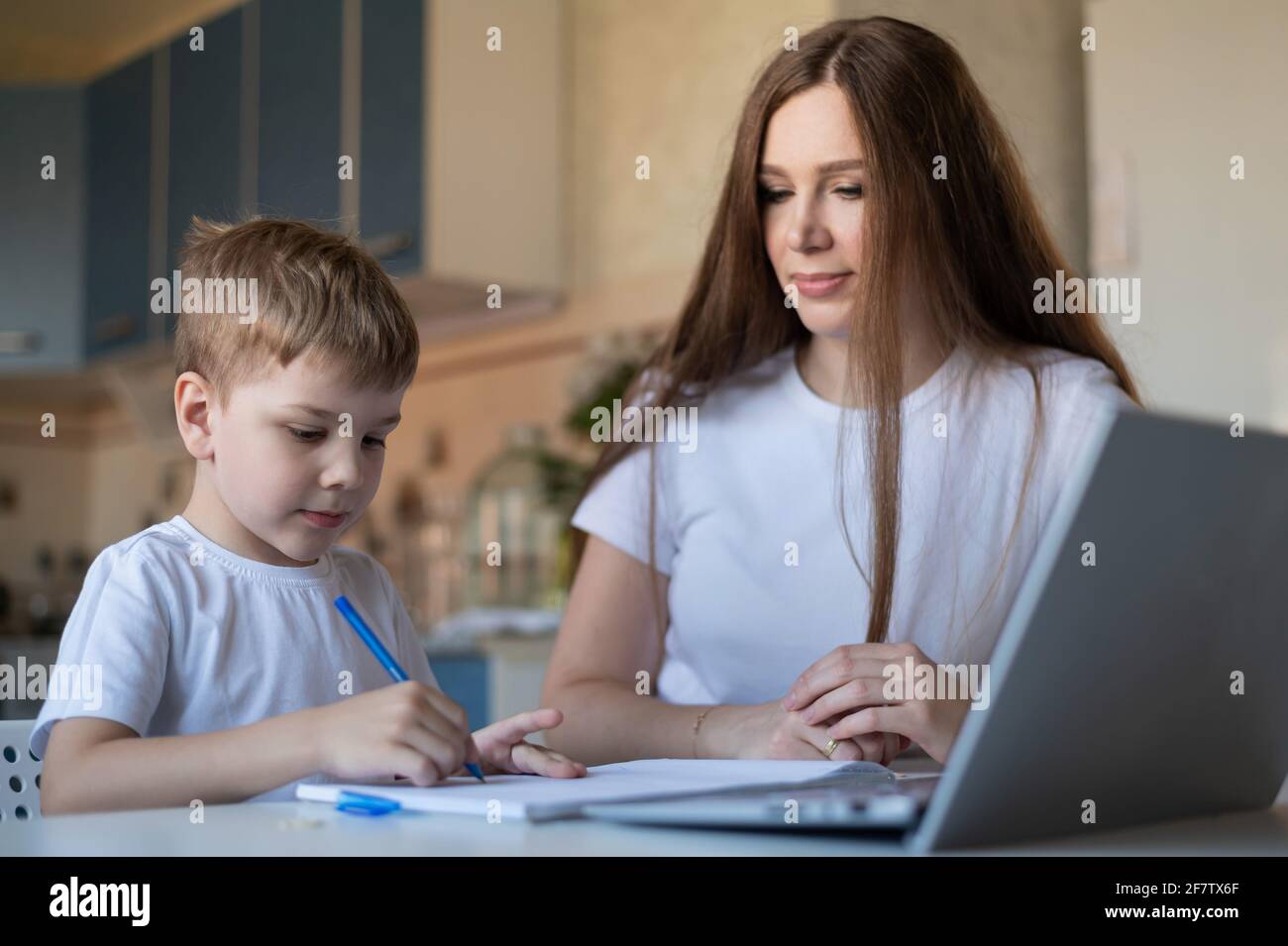 Donna caucasica aiuta suo figlio a imparare le lezioni. La madre che si prende cura controlla i compiti del bambino. Studio a casa durante la quarantena. Foto Stock