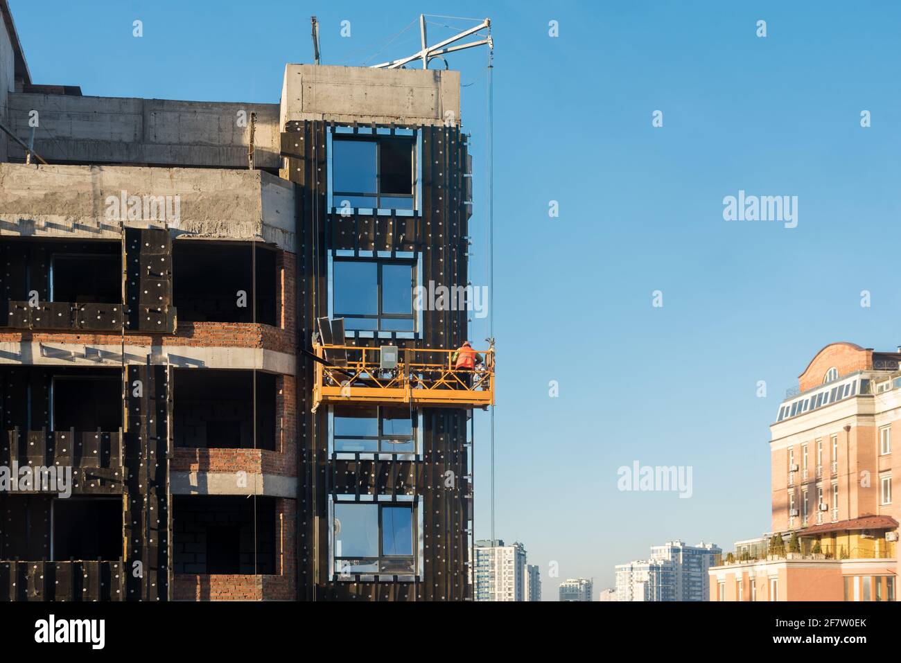 Lavori di costruzione di alto livello. Lavoratori del cantiere in culle che lavorano con la facciata. Culla sospesa per lavori all'esterno del grattacielo. B Foto Stock