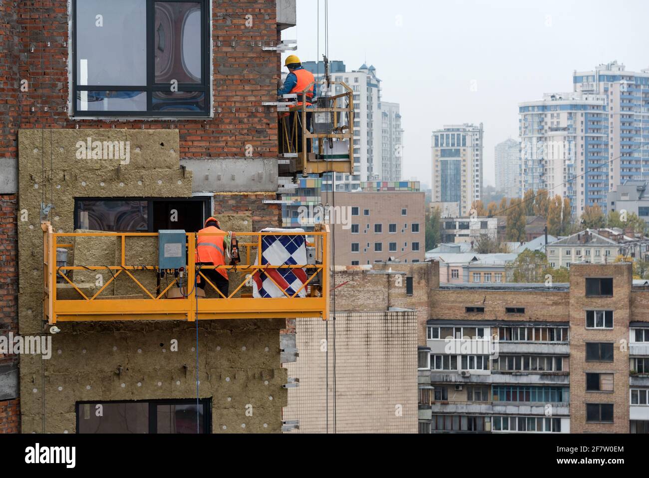 Lavori di costruzione di alto livello. Lavoratori del cantiere in culle che lavorano con la facciata. Culla sospesa per lavori all'esterno del grattacielo. B Foto Stock