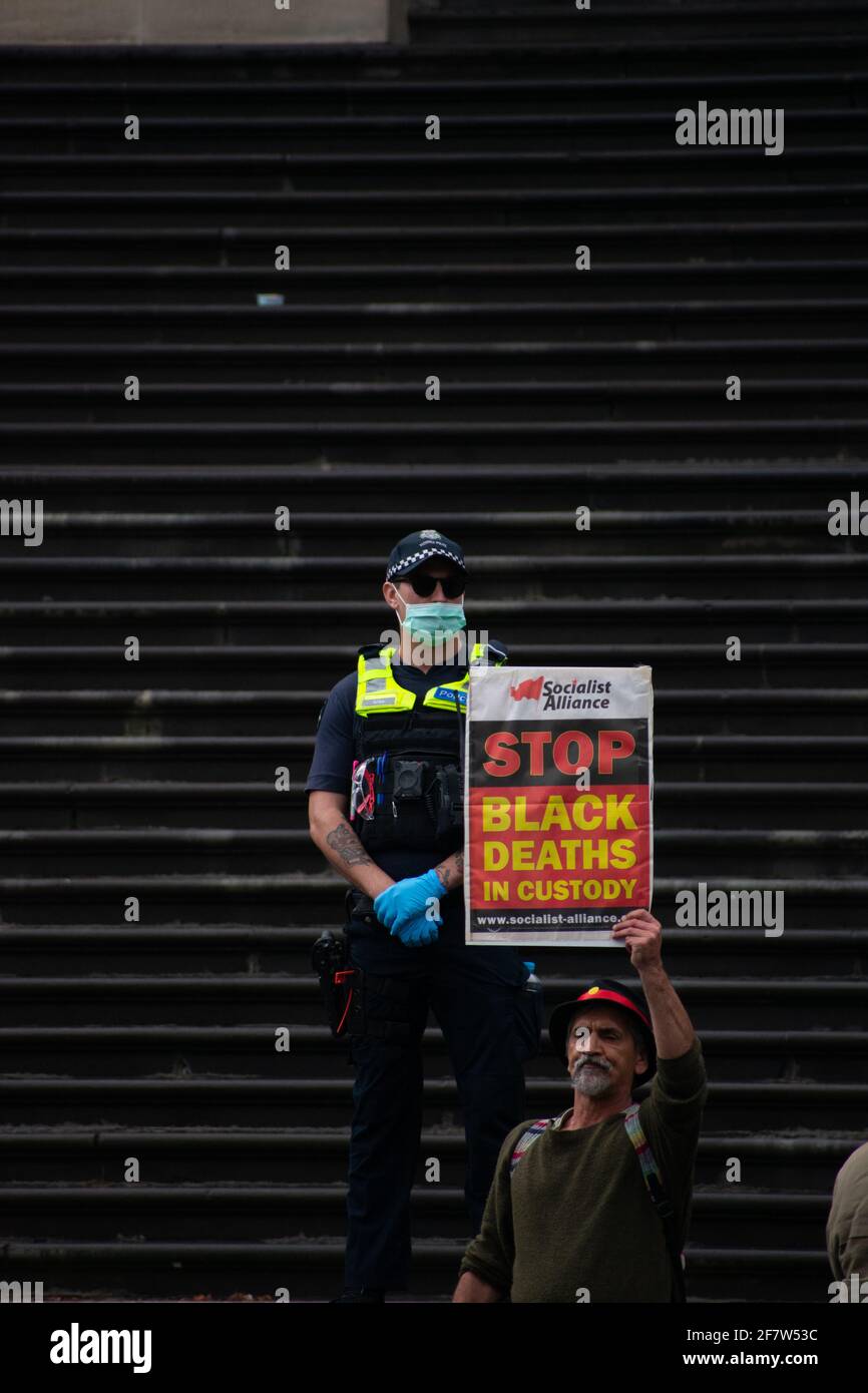 Melbourne, Australia. 10 aprile 2021. Un ufficiale di polizia si trova sui gradini fuori dal Parlamento, mentre un uomo aborigeno ha un cartello con la scritta "Salto i morti neri in custodia". Questo segue il caso più recente documentato di brutalità della polizia nei confronti di un adolescente aborigeno nel nuovo Galles del Sud all'inizio di questo mese. Credit: Jay Kogler/Alamy Live News Foto Stock