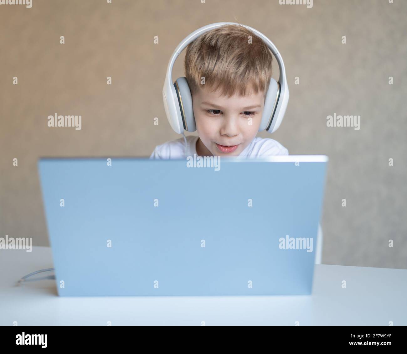 Cute Little boy sta guardando i cartoni animati o un film su un computer portatile. Il bambino caucasico si siede a un tavolo a casa e ascolta la musica con le cuffie. Foto Stock