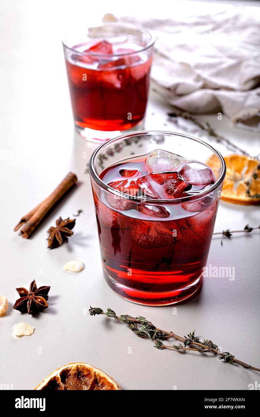 Primo piano cocktail freddo con vino di ciliegia. Bevanda alcolica ancora vita. Arance secche, bastoncini di cannella, origano, anice e zenzero secco. Sfondo chiaro. Ve Foto Stock