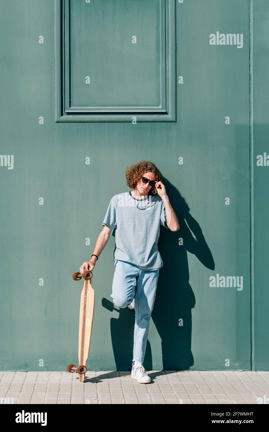 ritratto verticale di un giovane attraente in piedi e che tiene il suo skateboard. Foto Stock