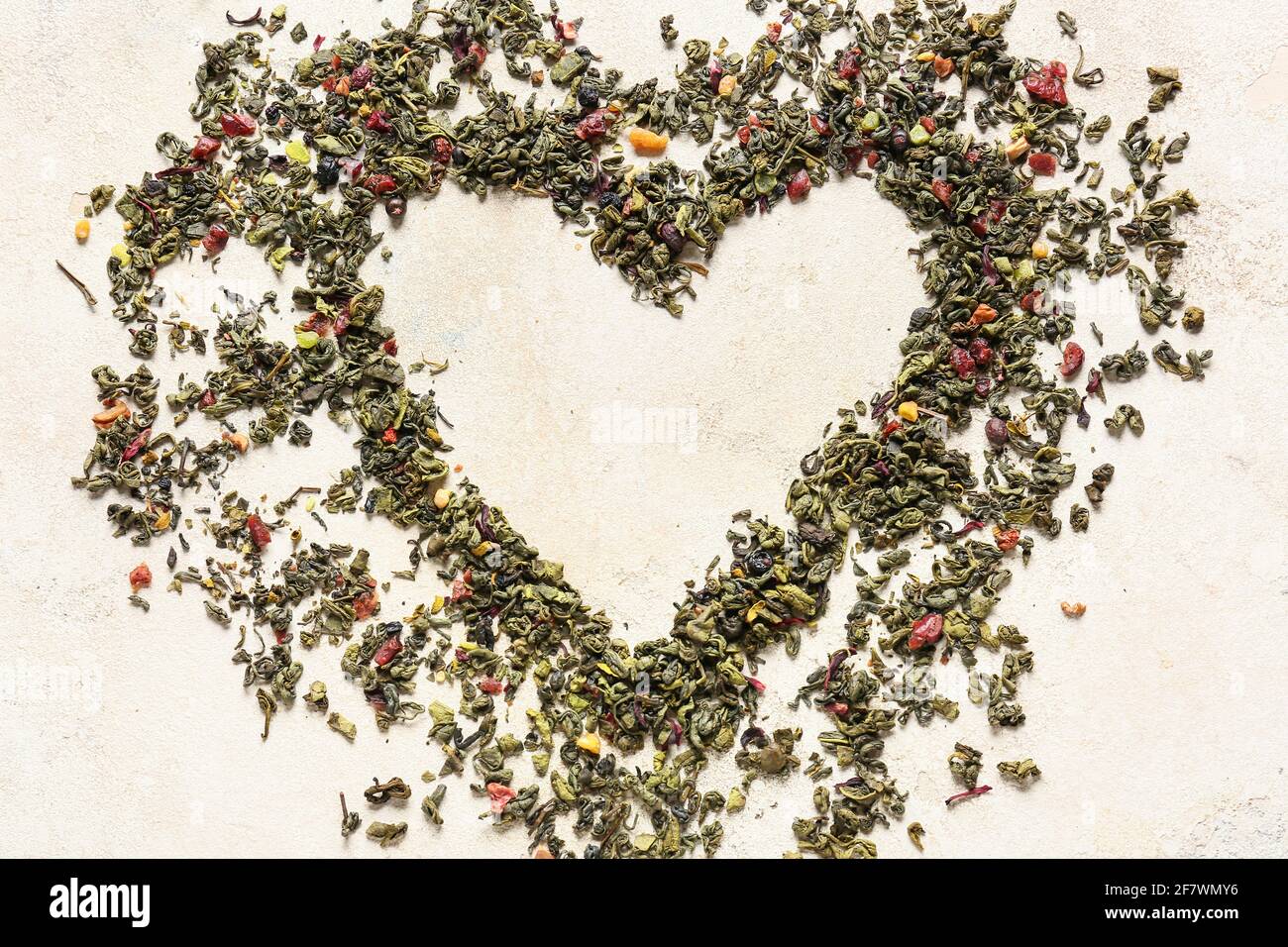 Forma del cuore fatta di tè verde secco su sfondo chiaro Foto Stock