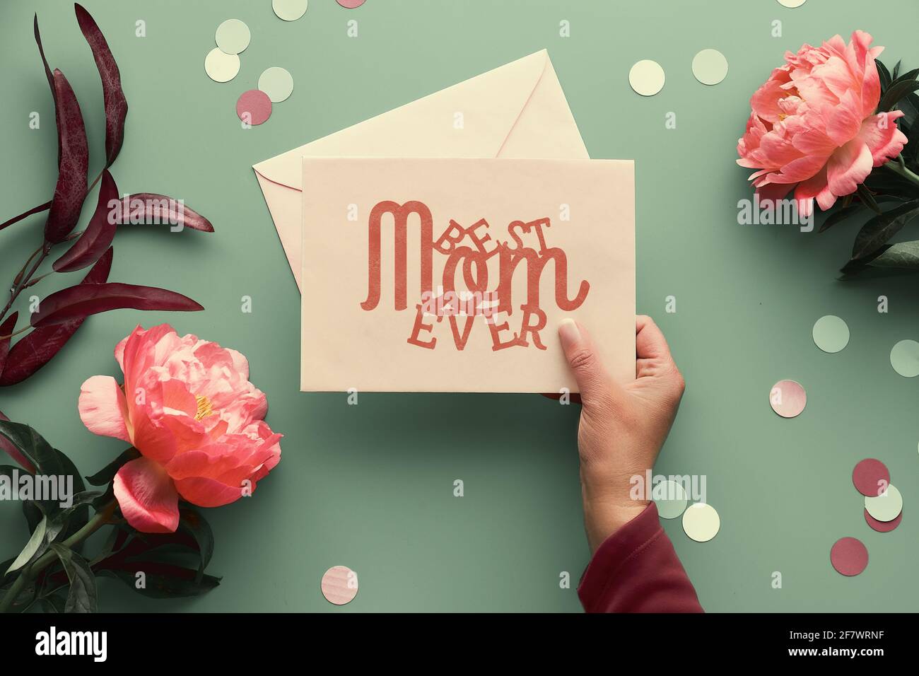 Design biglietto d'auguri per il giorno della mamma. Fiori di peonia rosa su sfondo verde sbiadito, testo migliore mamma mai su carta di carta con busta. Alla moda casual naturale Foto Stock