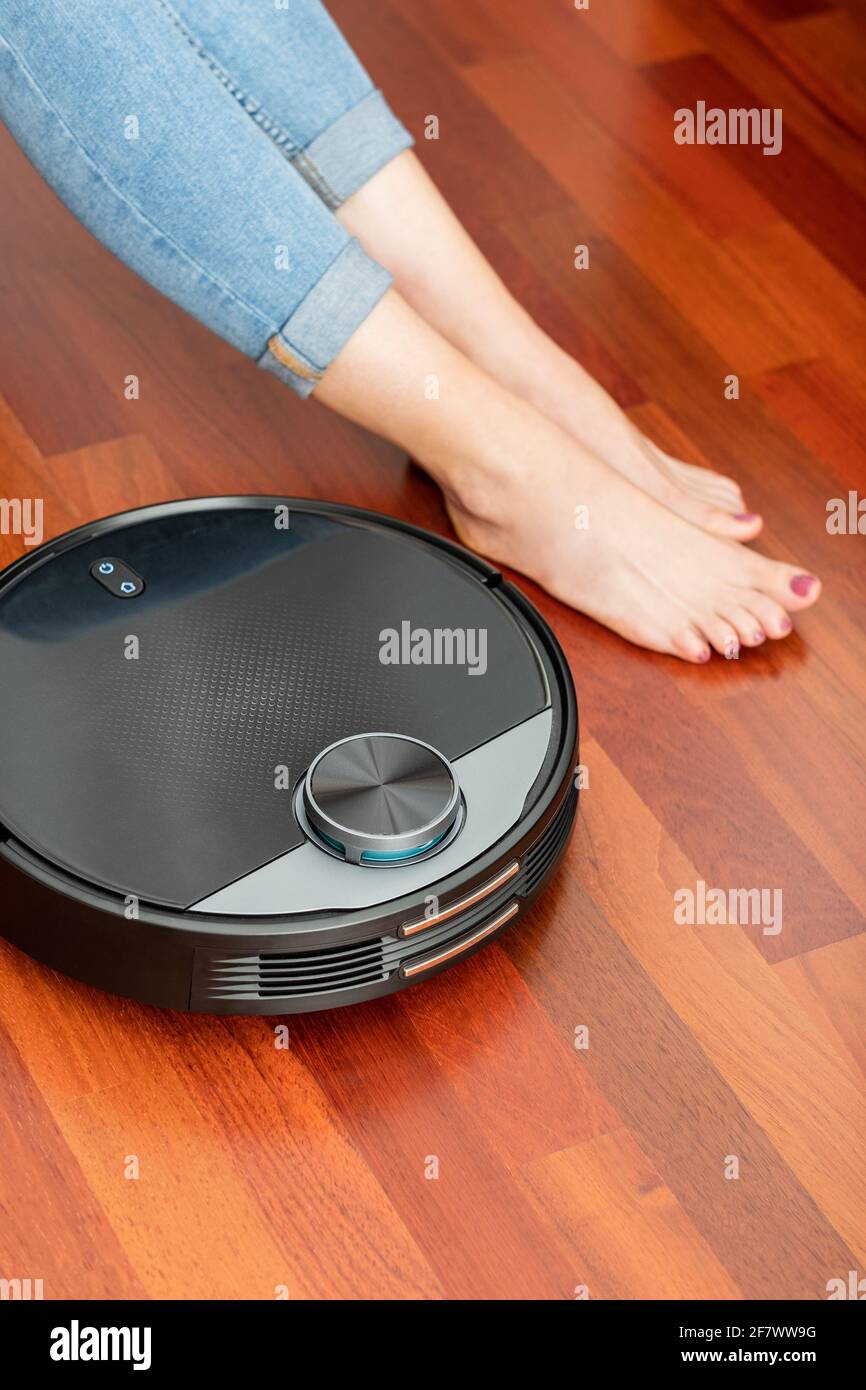 I piedi della ragazza giovane quando un aspirapolvere automatico  intelligente rotondo passa per pulire il pavimento, controllando il robot  della macchina per le attività domestiche Foto stock - Alamy