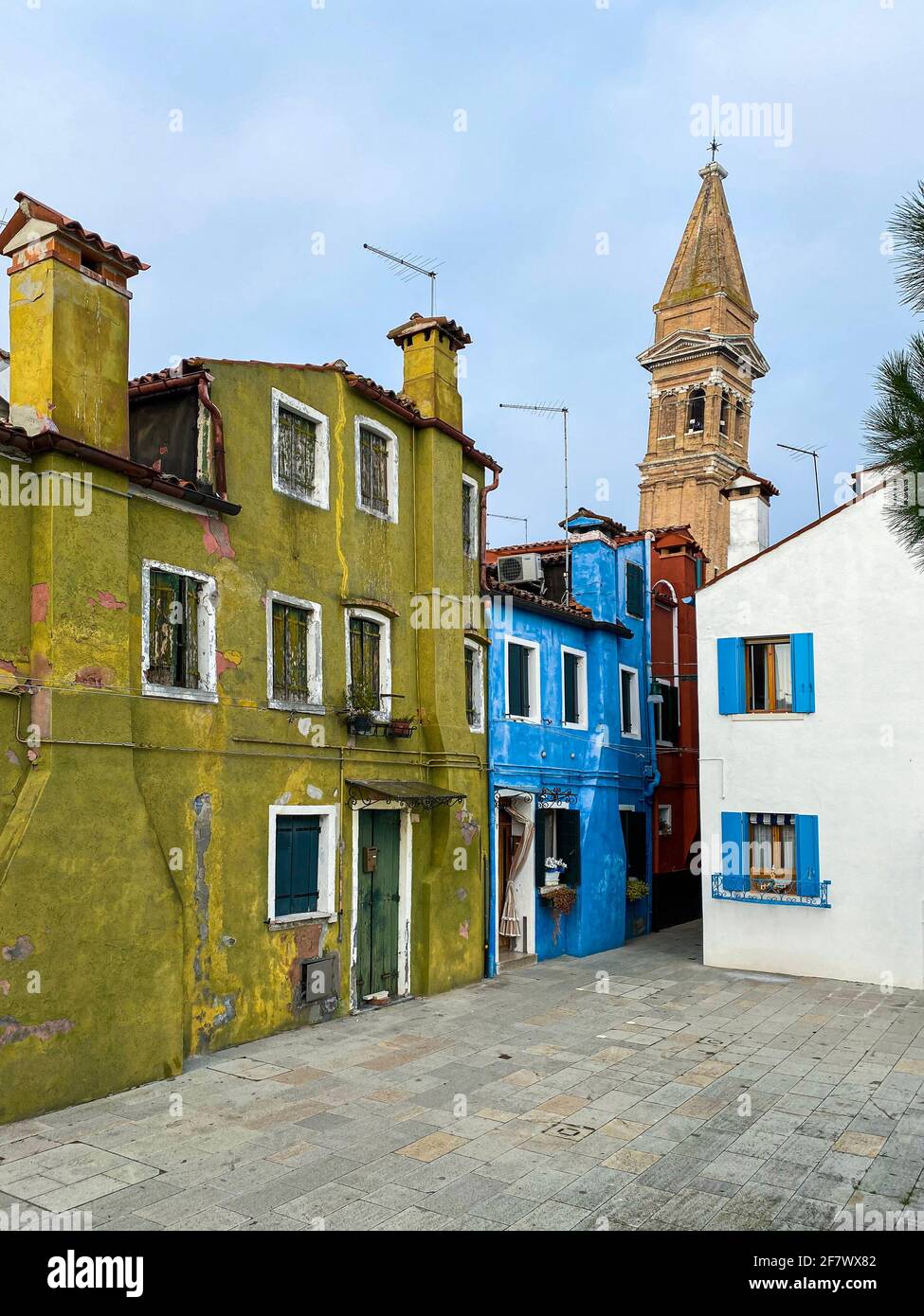 Case colorate su una piccola strada tradizionale con la cima di una chiesa che pende sull'isola di Burano, Venezia, Italia Foto Stock