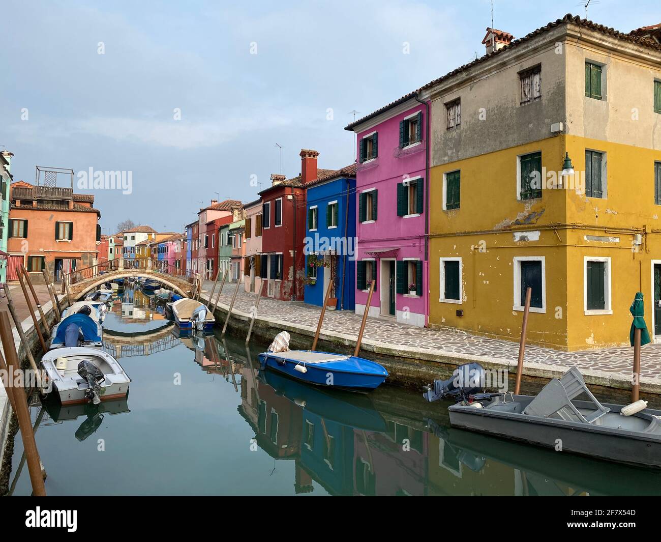 Barche ormeggiate e case colorate in una strada canale case sull'isola di Burano, Venezia, una gente irriconoscibile sullo sfondo. Foto Stock