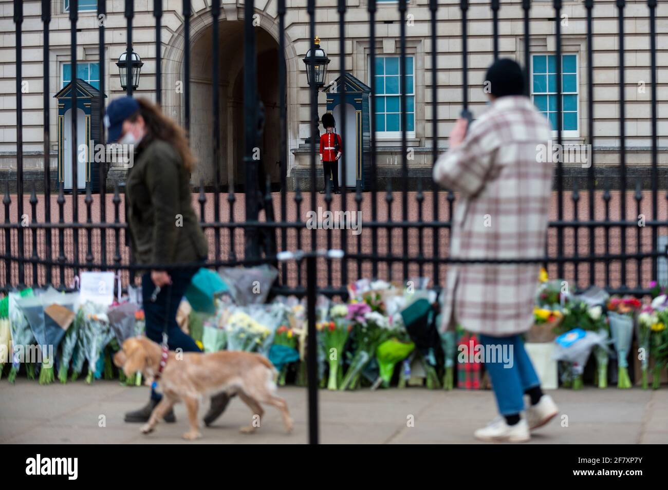 Londra, Regno Unito. 10 aprile 2021. Un membro della guardia di vita della regina guarda sopra così come i wishers lasciano i fiori fuori Buckingham Palace dopo che la morte del principe Filippo, 99 anni, è stata annunciata il giorno precedente. Credit: Stephen Chung / Alamy Live News Foto Stock