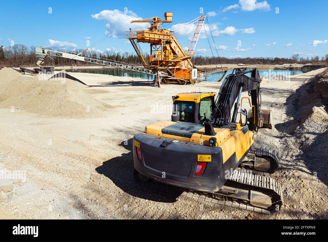 Draga mobile di ghiaia arancione e un scavatore di pala in uno stagno di cava alla luce del sole, Baviera, Germania Foto Stock