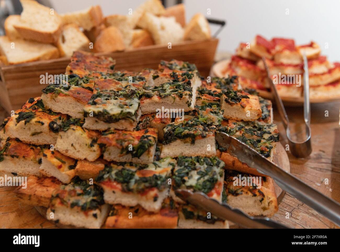 Fette di pizza a forma quadrata con crosta morbida su a. tavolo con tong da cucina Foto Stock