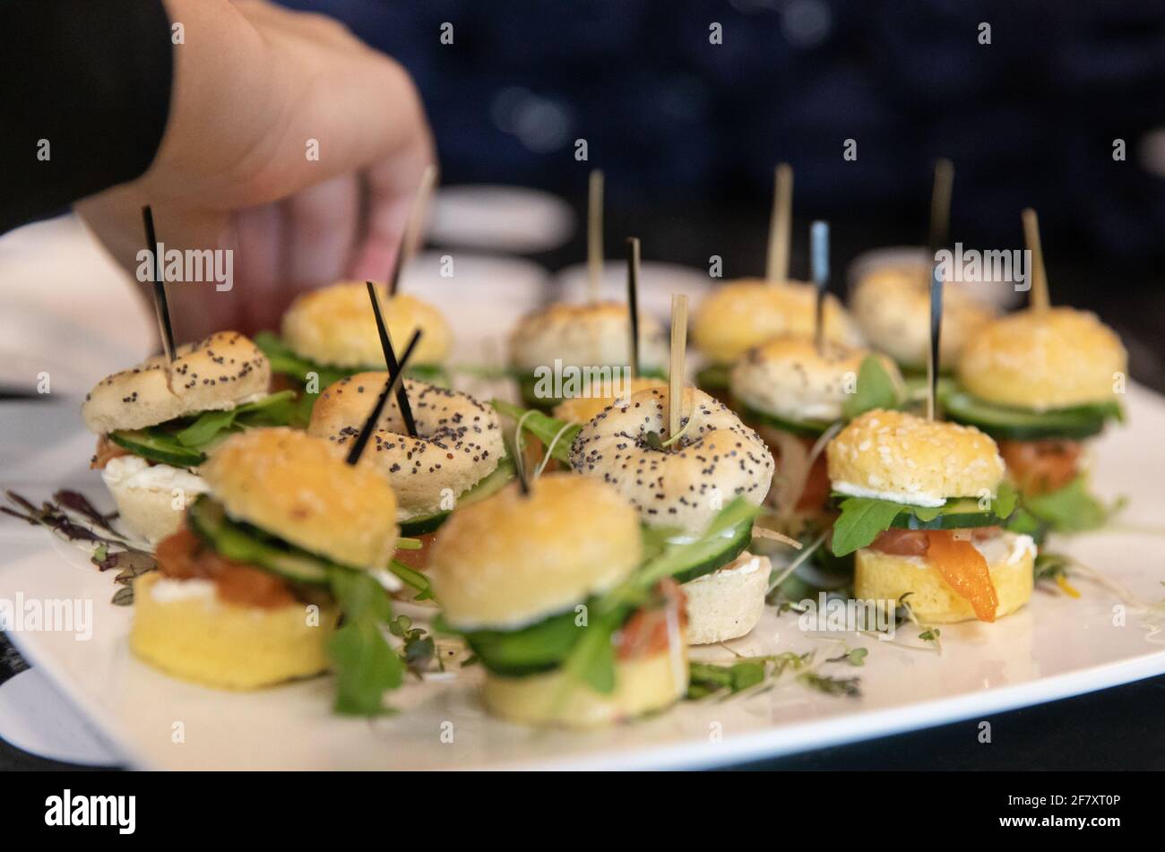Piccolo sandwich di pane al sacco con papavero e sesamo semi su un piatto bianco con una mano che raggiunge giù per uno Foto Stock
