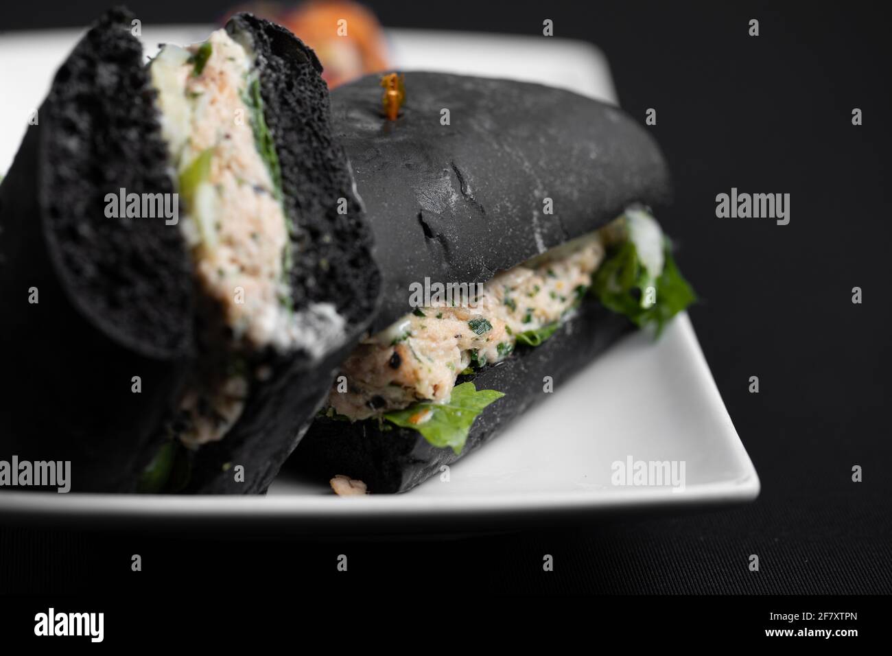 panino di pane nero affettato a metà servito su un bianco piastra quadrata Foto Stock