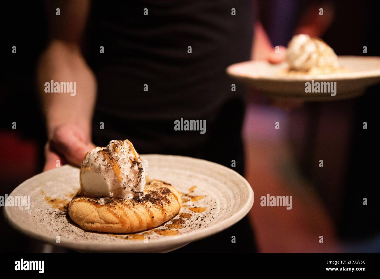 l'uomo caucasico è un server in un ristorante che ne detiene due piatto bianco rotondo con pasticceria e gelato alla vaniglia sopra con un po' di zucchero Foto Stock