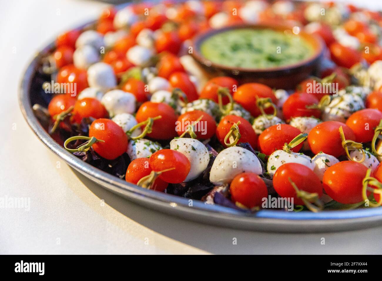 Pomodori ciliegini e palle di formaggio su un bastone presentato sopra una piastra rotonda in metallo con salsa al centro Foto Stock