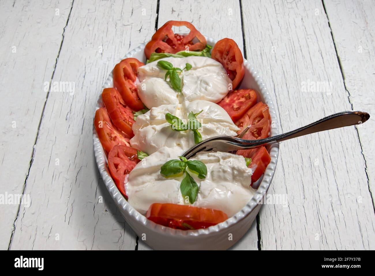 Insalata caprese italiana con mozzarella di bufala, basilico, olio d'oliva su fondo bianco di legno. Vista dall'alto Foto Stock