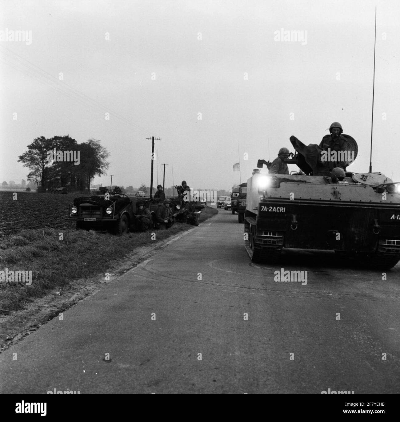 Soldati olandesi in copertura a due DKW Mungas della Royal Netherlands Army lungo il lato di una strada di campagna durante un esercizio internazionale a Westfalia, Germania occidentale. Passa un camion blindato britannico Foto Stock