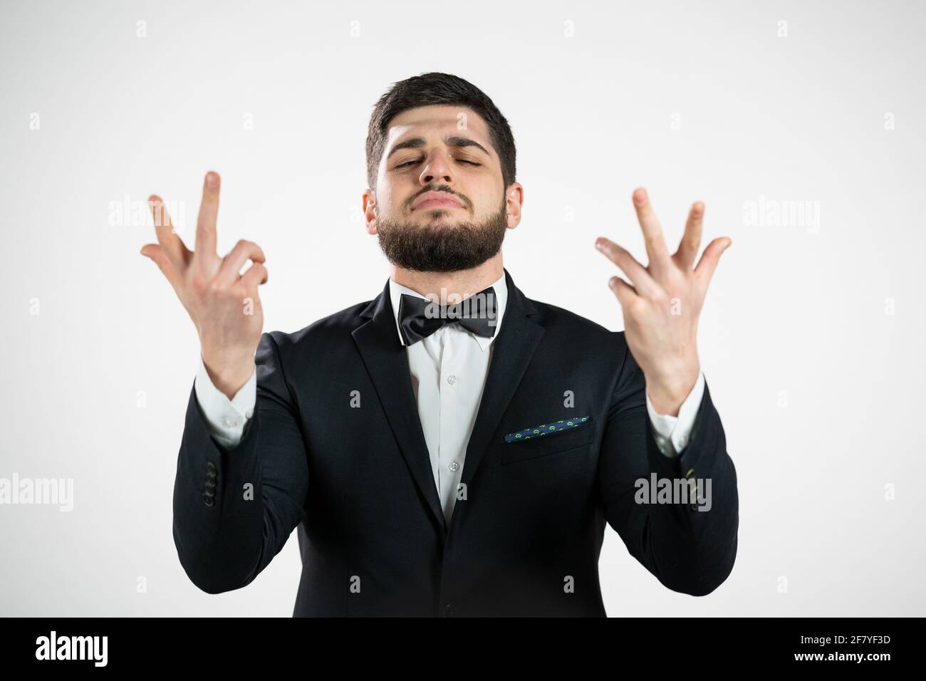 Giovane che fa un gesto delizioso e perfetto. Ragazzo con barba in tuxedo ammira il gusto della cucina italiana su sfondo bianco studio. Concetto di belissimo. Foto Stock