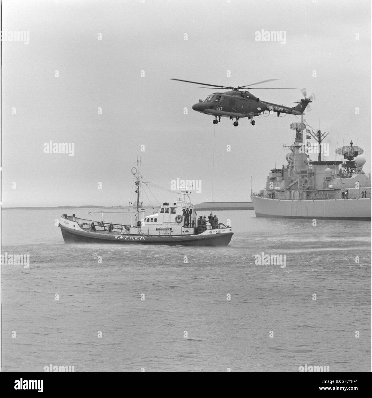 Persona fisica trasporto da una piattaforma galleggiante da parte del Westland SH-14D Navy Lynx Helicopter con registrazione 283 (1981-ca 2012) in collaborazione con la luminosa barca di salvataggio Suzanna (1968-1998) della Royal North e South Holland Redding Company (Knzhrm) nel maggio 1990.rechts, si trova L-Fregat HR.MS. White De con (1986-2005) nel porto di Den Helder. Foto Stock