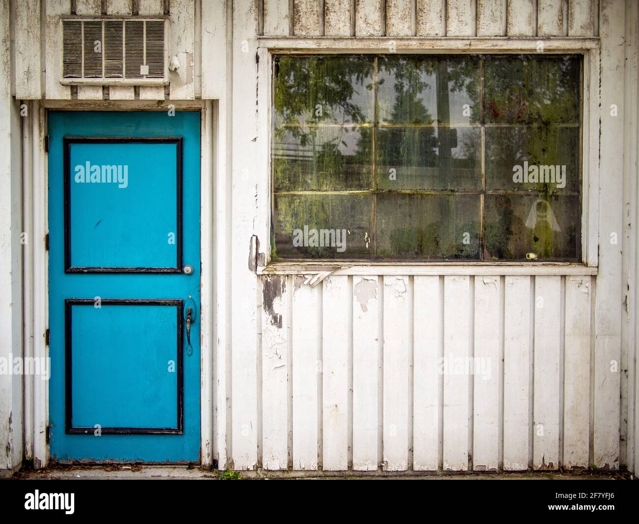 Porta turchese su un muro con una finestra rotta la facciata di una casa abbandonata Foto Stock