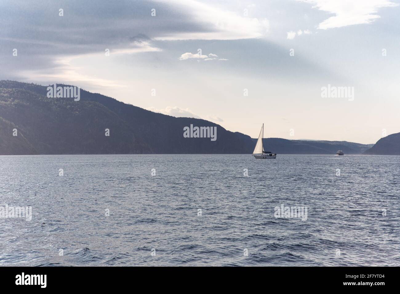 Barca a vela che galleggia sull'acqua in estate con un montagna in lontananza e nuvole nel cielo Foto Stock