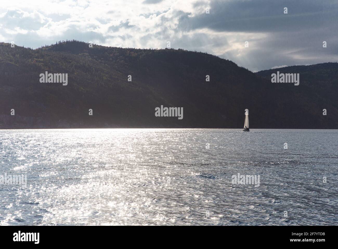 barca a vela sull'acqua con una silhouette di montagna scura dentro lo sfondo Foto Stock