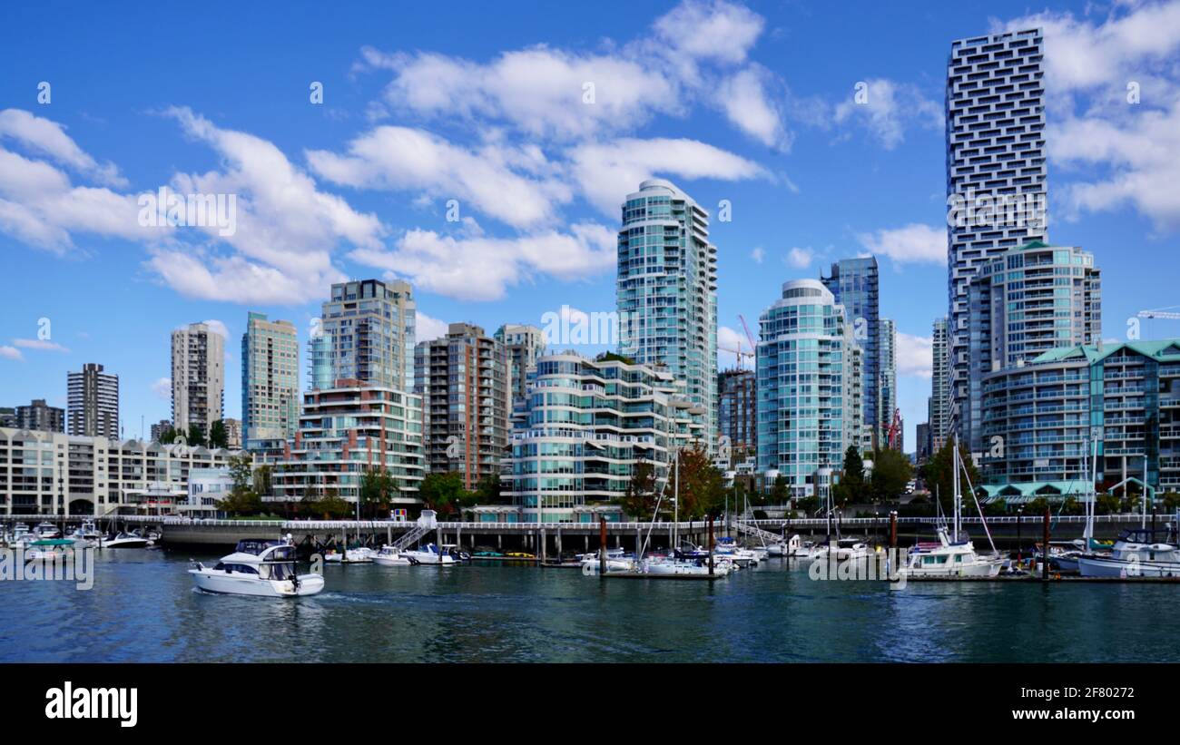 Un sacco di canali attraccati da molo a Granville Island di Vancouver, Canada, con alta buidling lontano e cielo blu sopra. Foto Stock