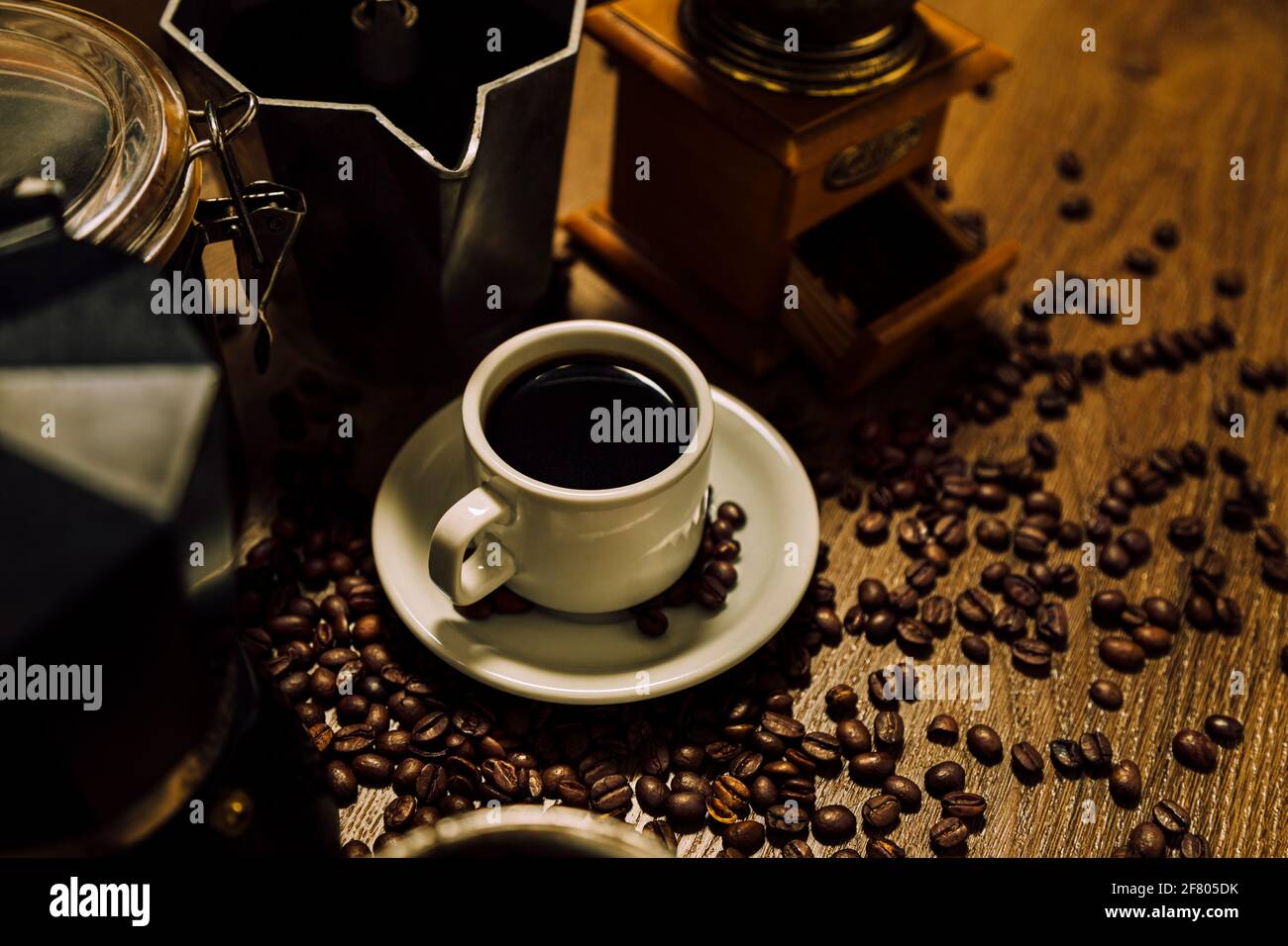 Roba di caffè. Una tazza bianca con caffè nero, moka italiana, un mulino e cereali su un tavolo di legno. Stile rustico vintage. Foto Stock