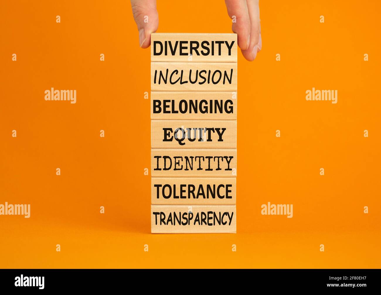 Diversità appartenenza inclusione equità tolleranza d'identità trasparenza parole scritte su blocco di legno. Mano maschio. Bellissimo sfondo arancione. Diversità, Foto Stock